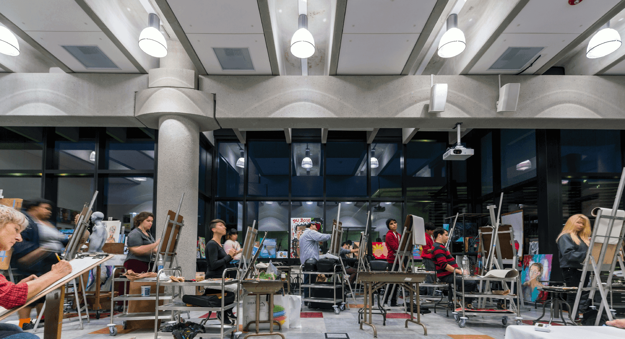 An art classroom with students sitting at easels set up with canvases on them.