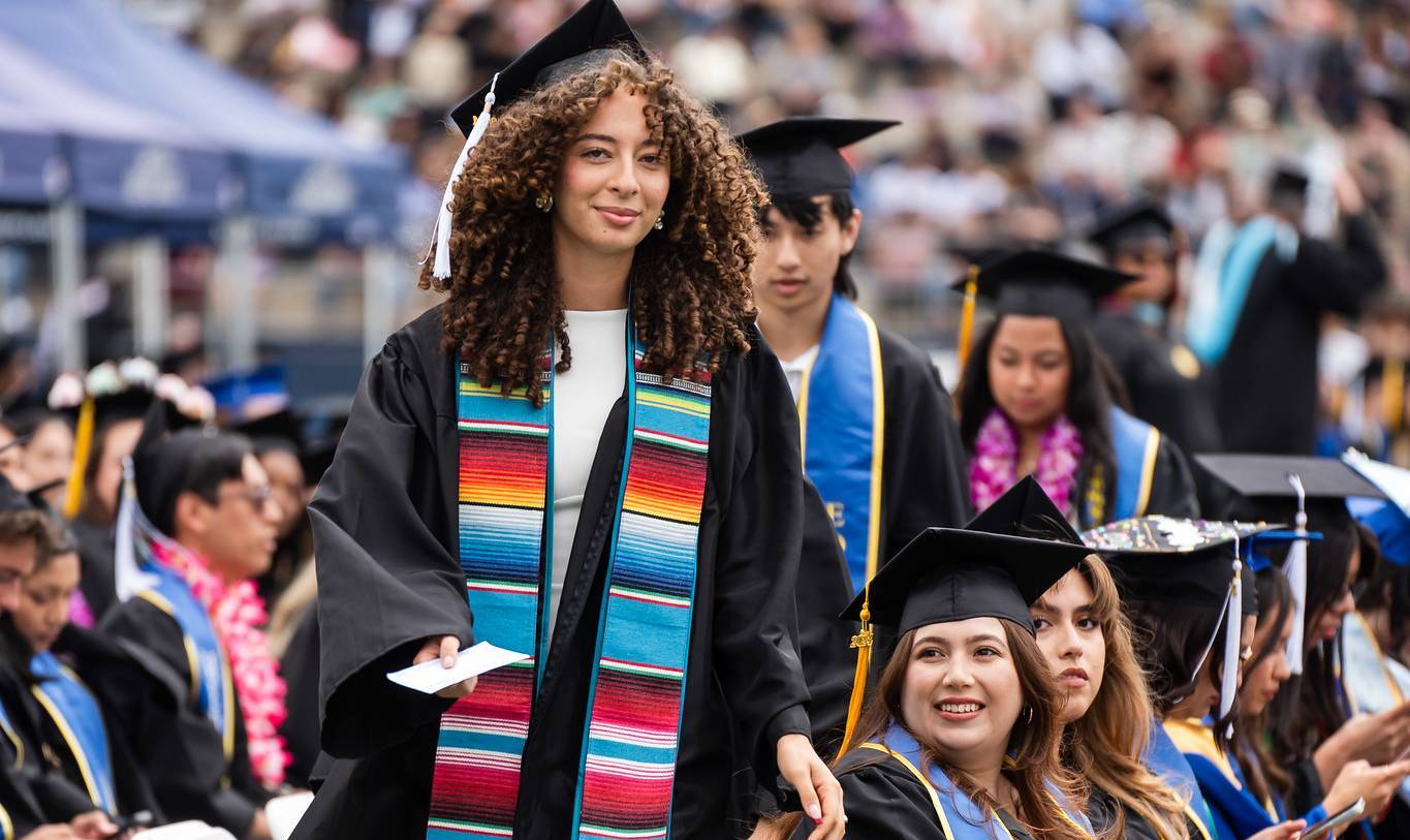 A student in a black graduation cap and gown wearing a colorful stole