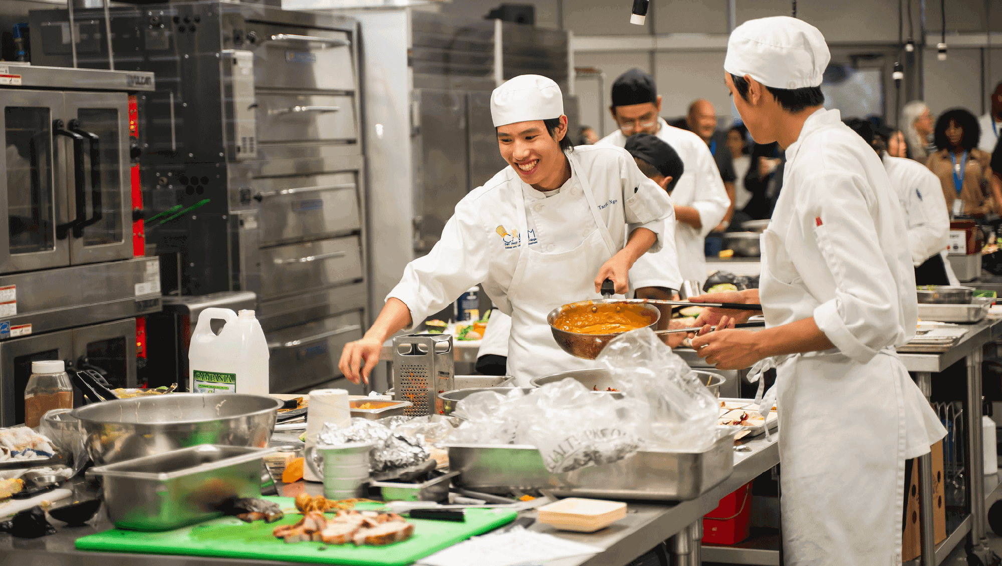 Two chefs working in a kitchen in white smoks and caps