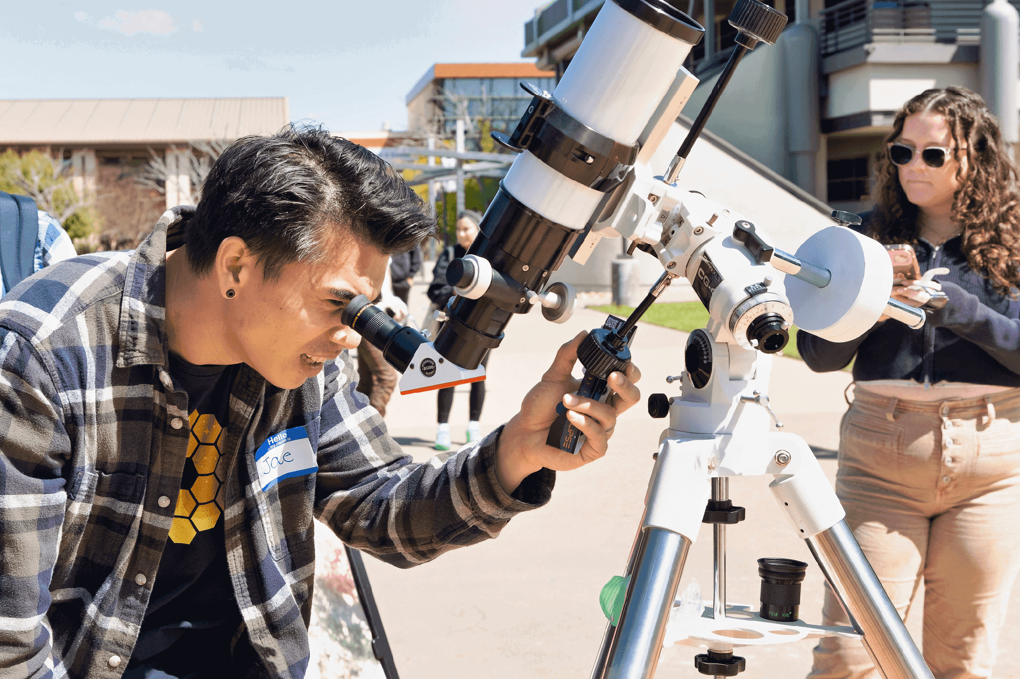 A student looks through a white telescope to see the eclipse.