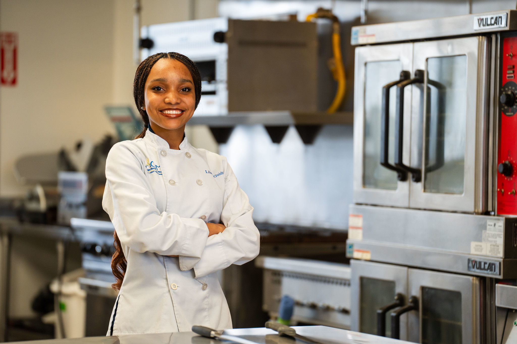 A student in a white chefs smock in a kitchen