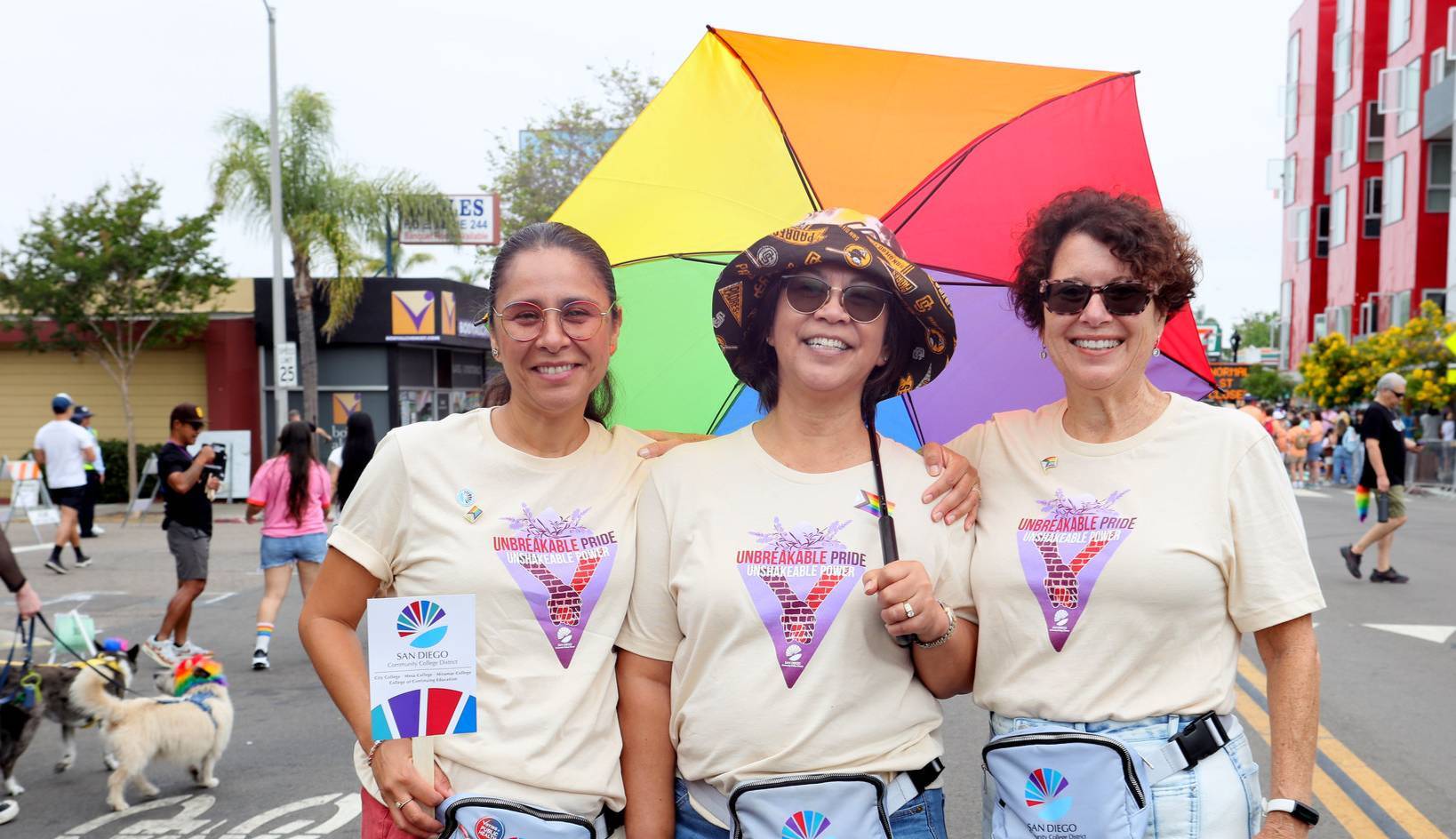 Two trustees and a vice chancellor at the pride parade. One is holding a rainbow umbrella.