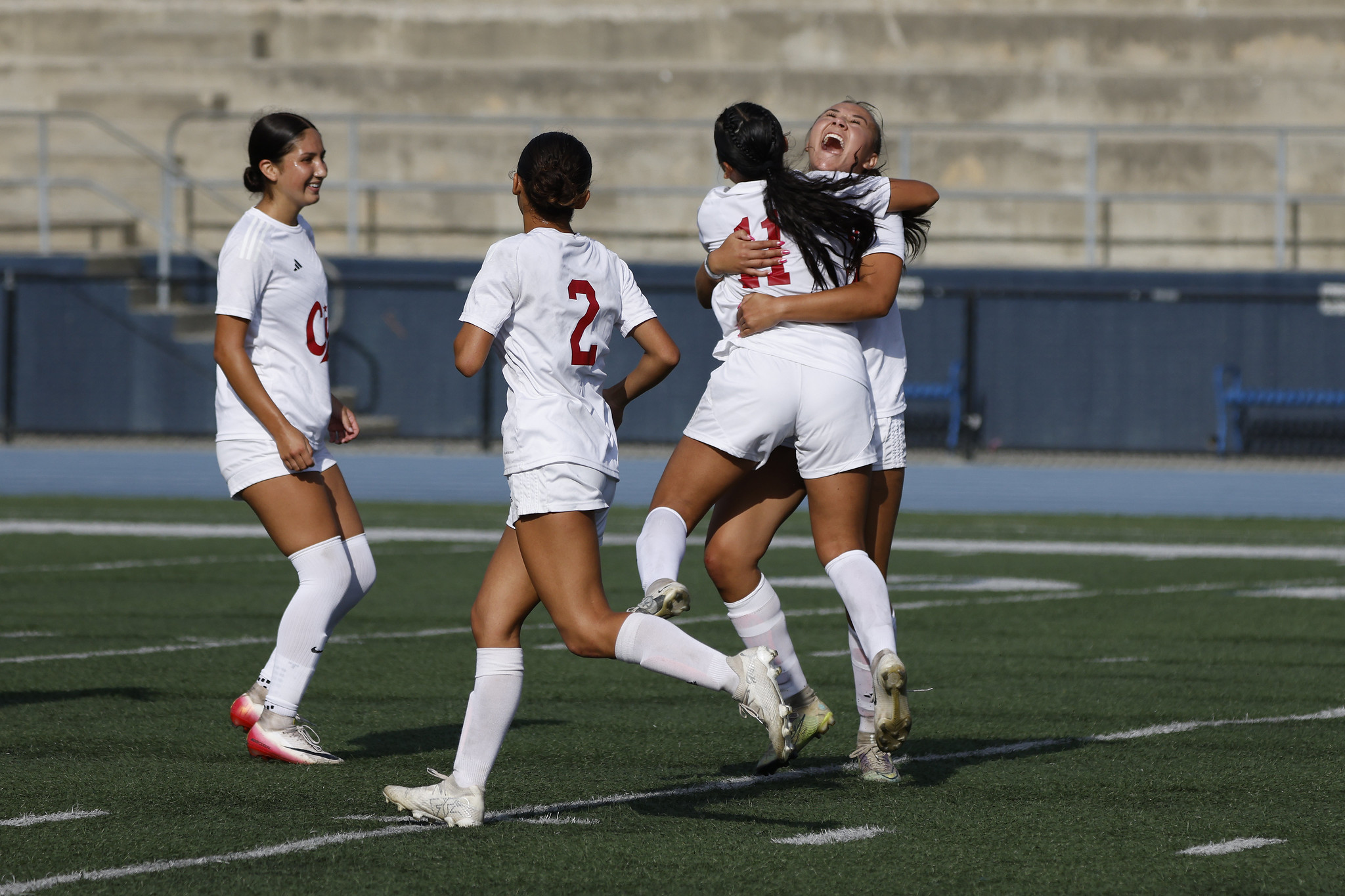 Two players on the womens soccer team hug. Two more are running past them.