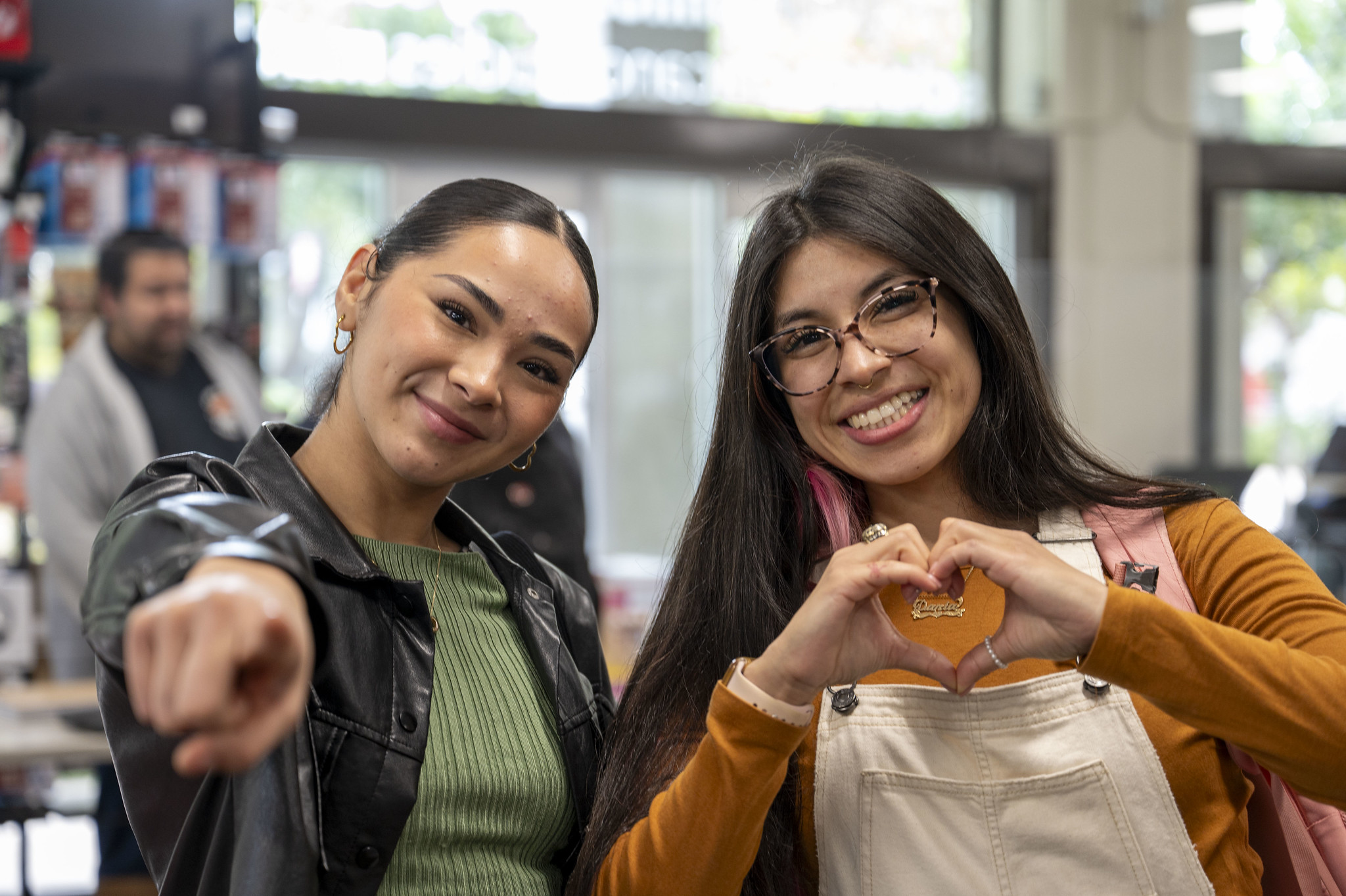One student points to the camera and another is making a heart sign with her hands
