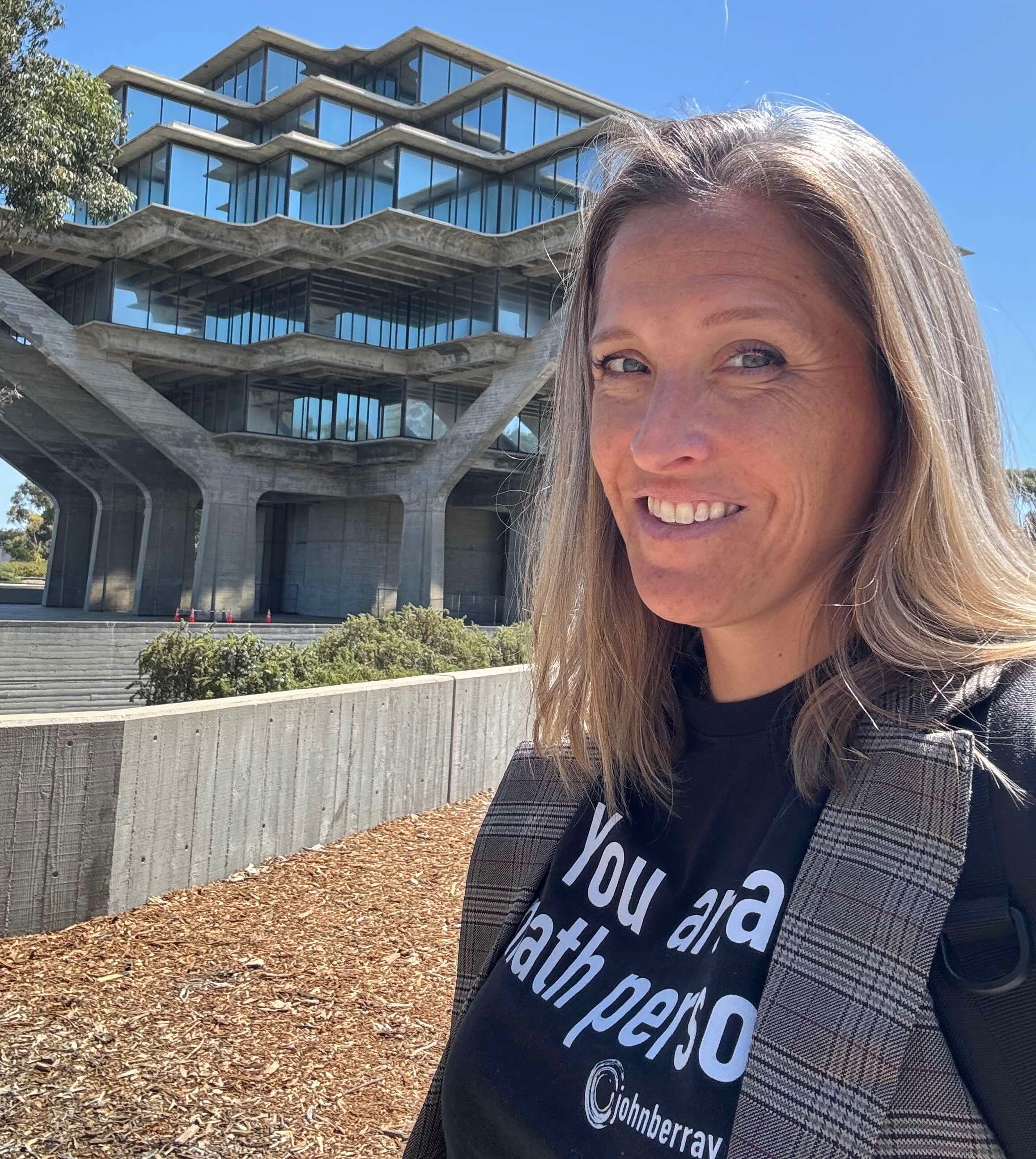Kelly, a white woman with shoulder-length light brown hair, smiles at the camera wearing a black shirt