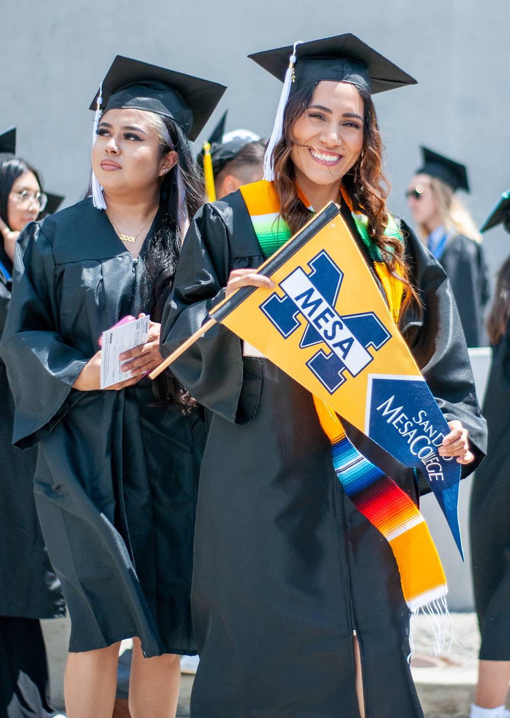 A student in a cap and gown holds up a banner at Mesa Commencement