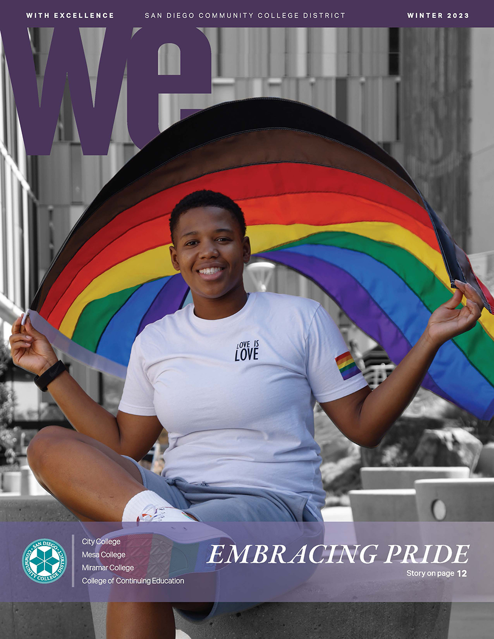 A student in a white tee shirt that says love is love is holding a rainbow flag above their head