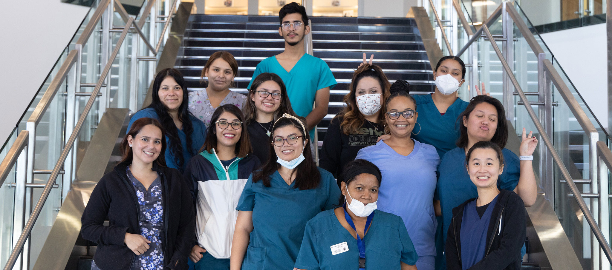 13 healthcare students in scrubs take a group photo on stairs