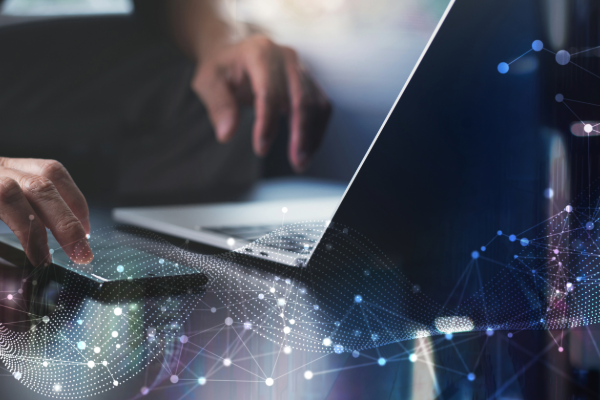 A pair of hands typing on a laptop with a smartphone next to the laptop