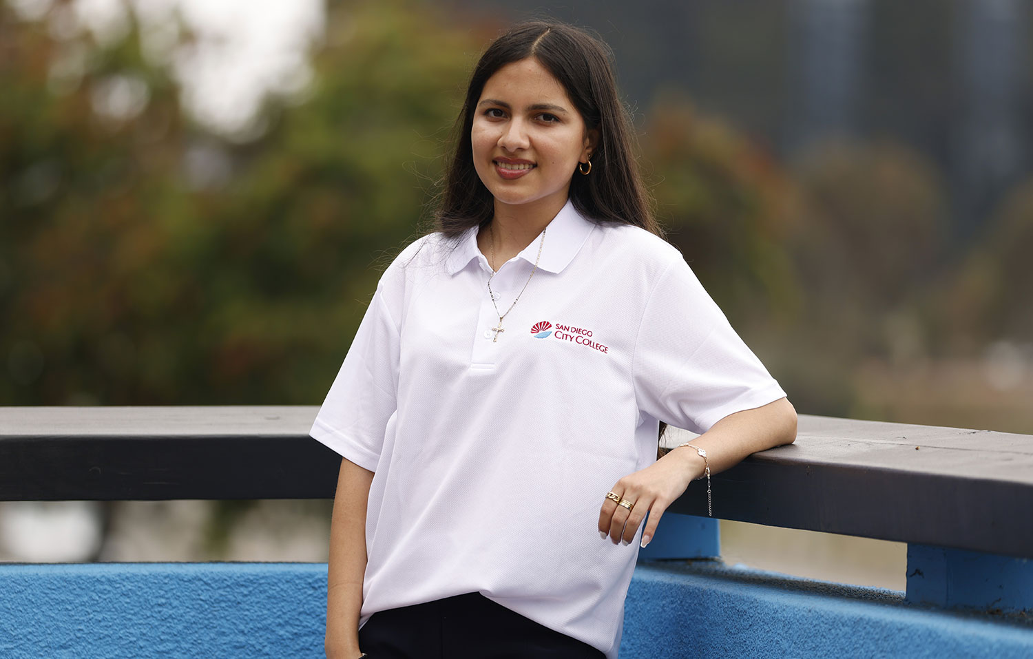 Celina Martinez wears a white City College polo shirt while standing outside on a balcony.