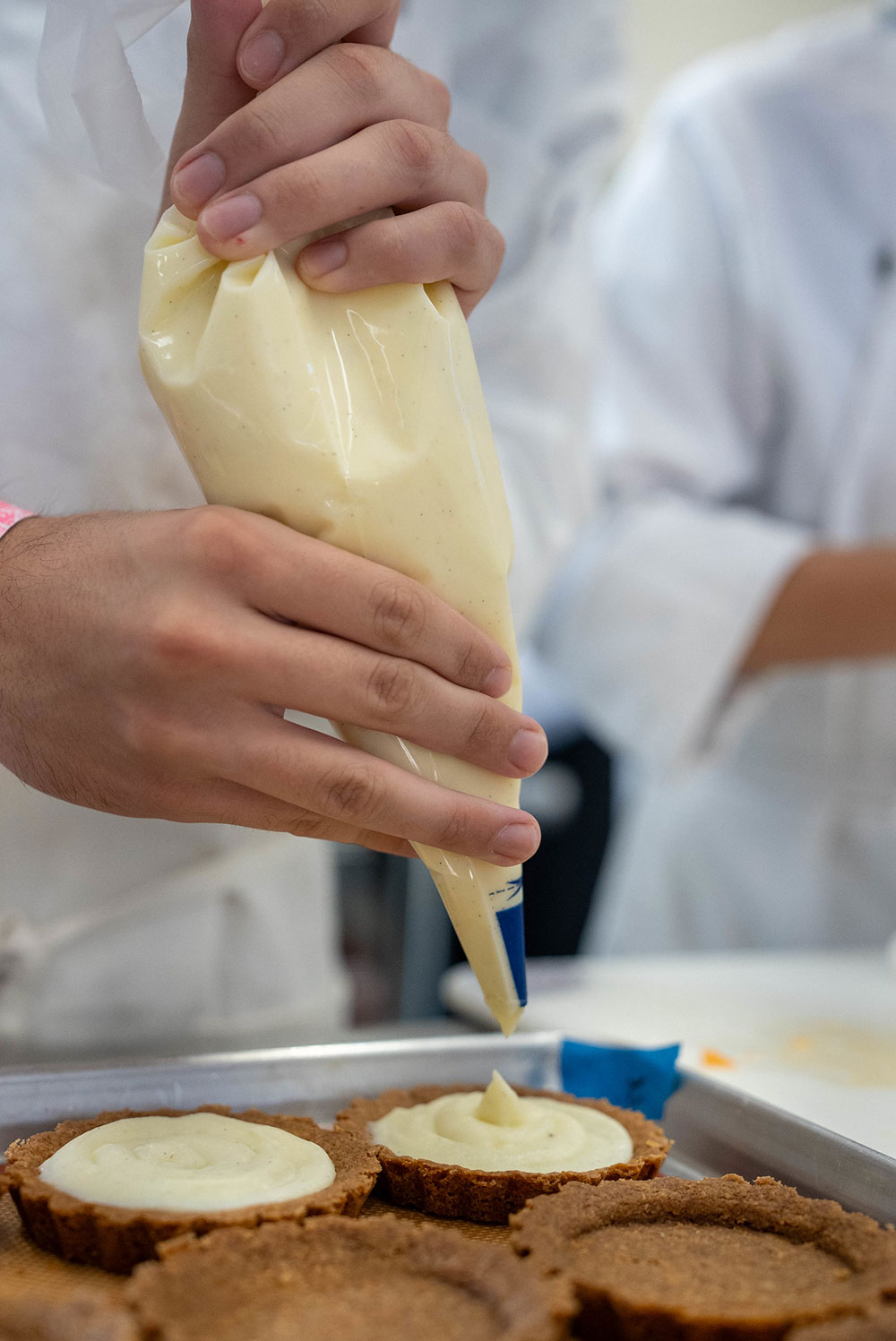 A student uses a piping bag to put custard into tart crusts