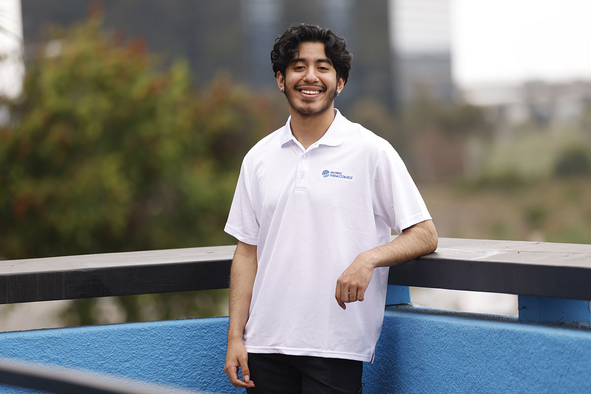 Jermiah Palomino wearing a white Mesa College polo and standing on a balcony