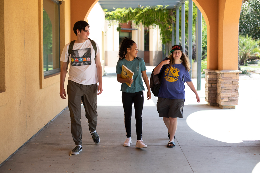 Three students walking through an archway with stone and orange walls, engaging in conversation.