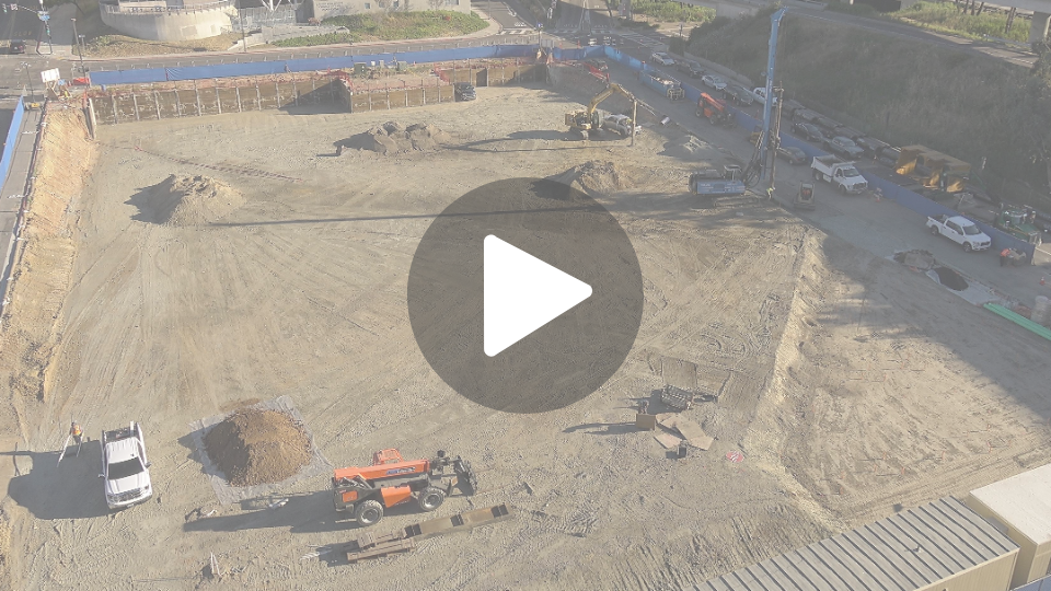 Construction site primarily showing flat dirt with construction vehicles spread throughout the site working. 
