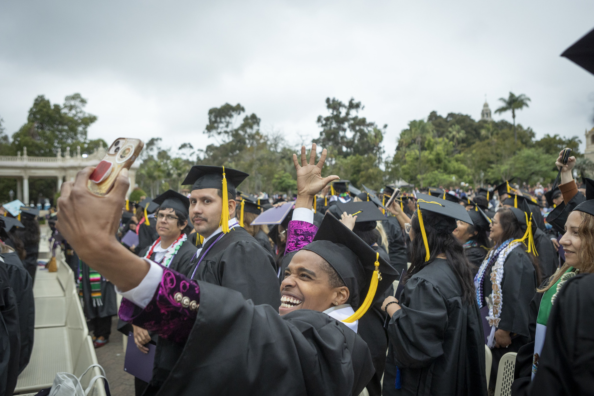 
A happy graduate takes a selfie whild surrounded by other graduates in the crowd.
