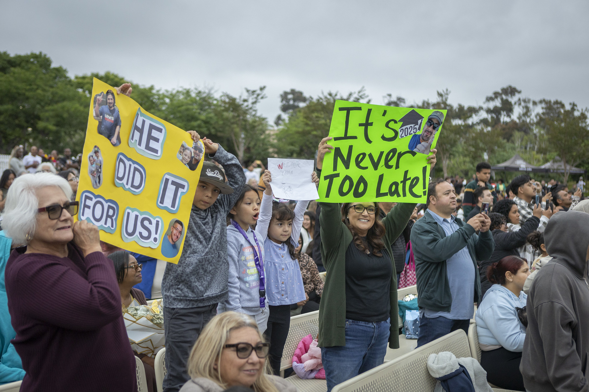 
Family and friends in the crowd holding two signs. One sign says he did it for us and the other says It's never too late.
