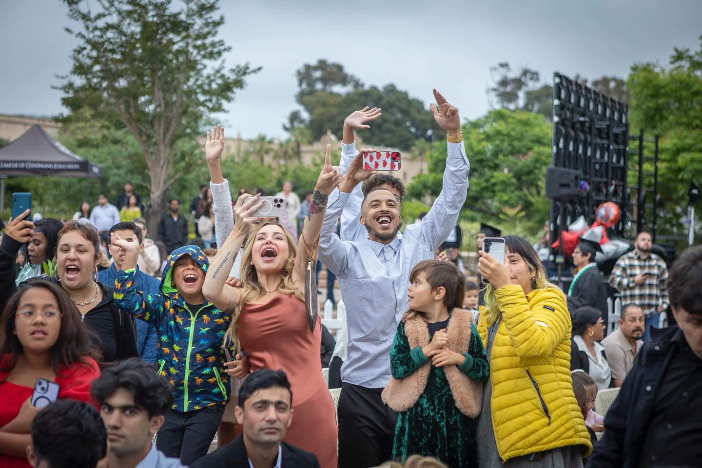 
Family and friends in the crowd cheering and taking picture with their cell phones.

