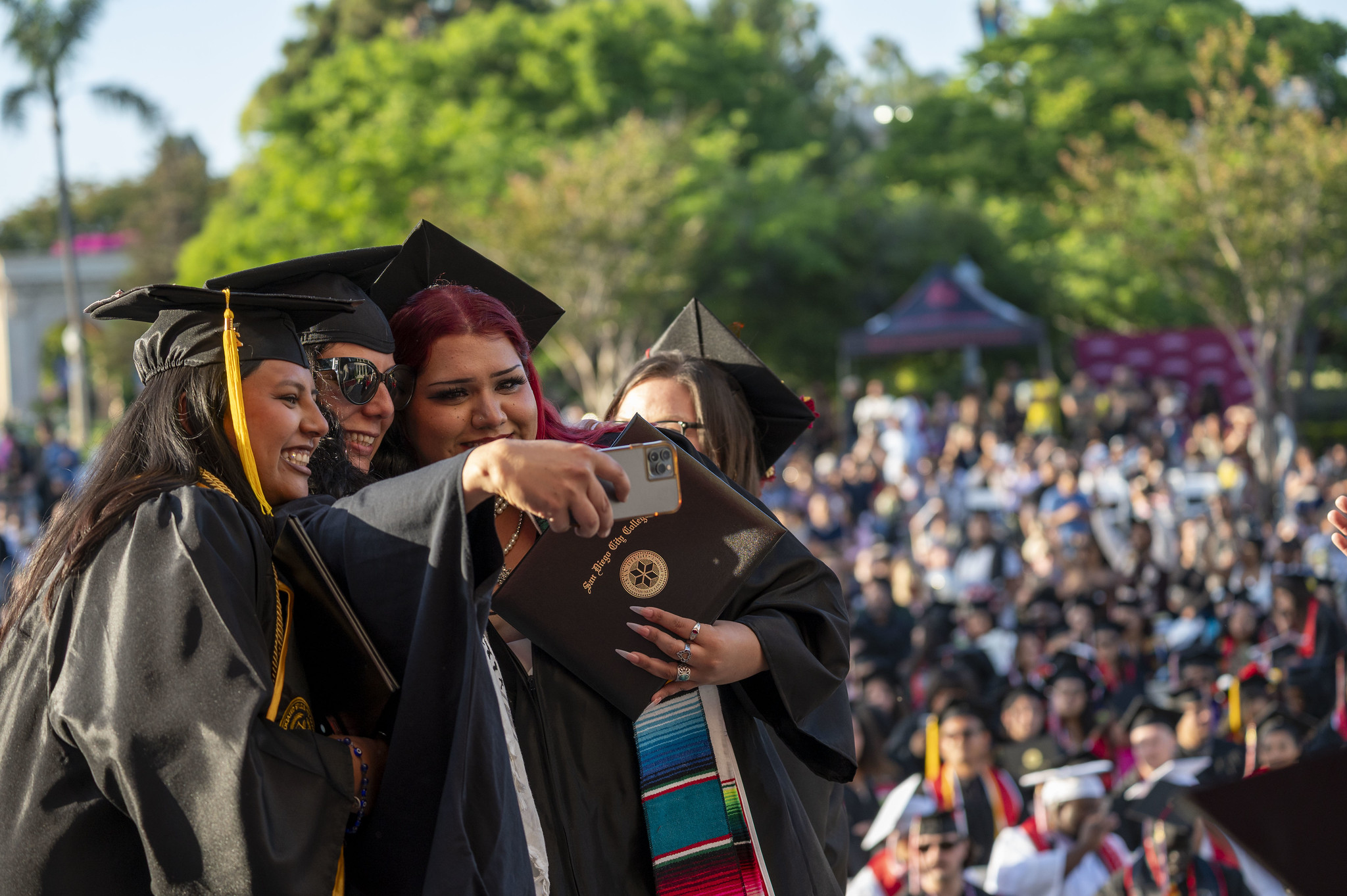 
Three graduates take a selfie on stage.
