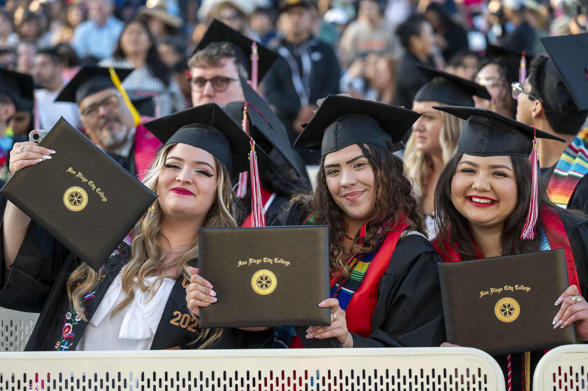 
Three graduates in the audience hold up their degrees.
