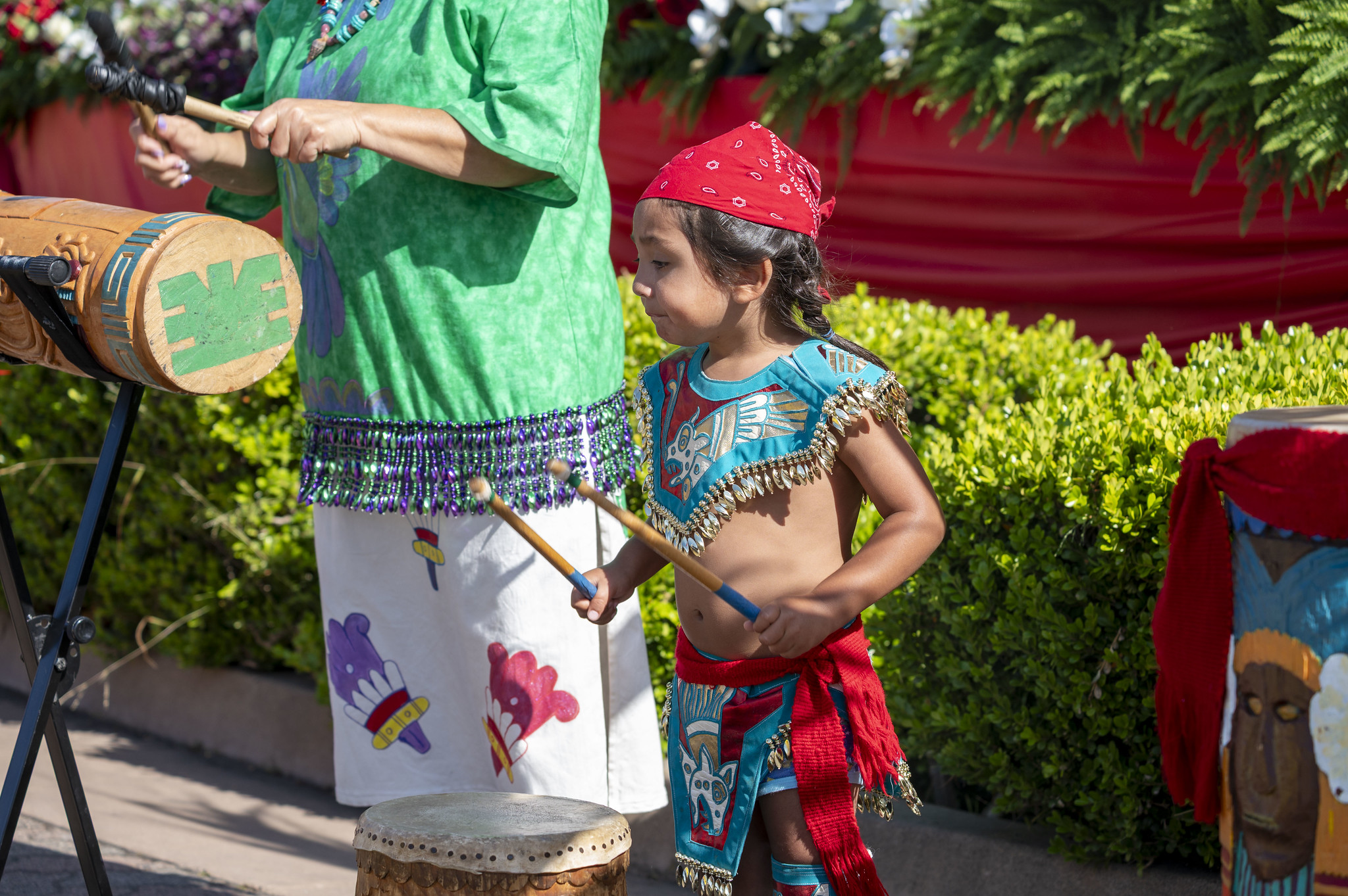 
A little boy in an Aztec costume plays a drum.
