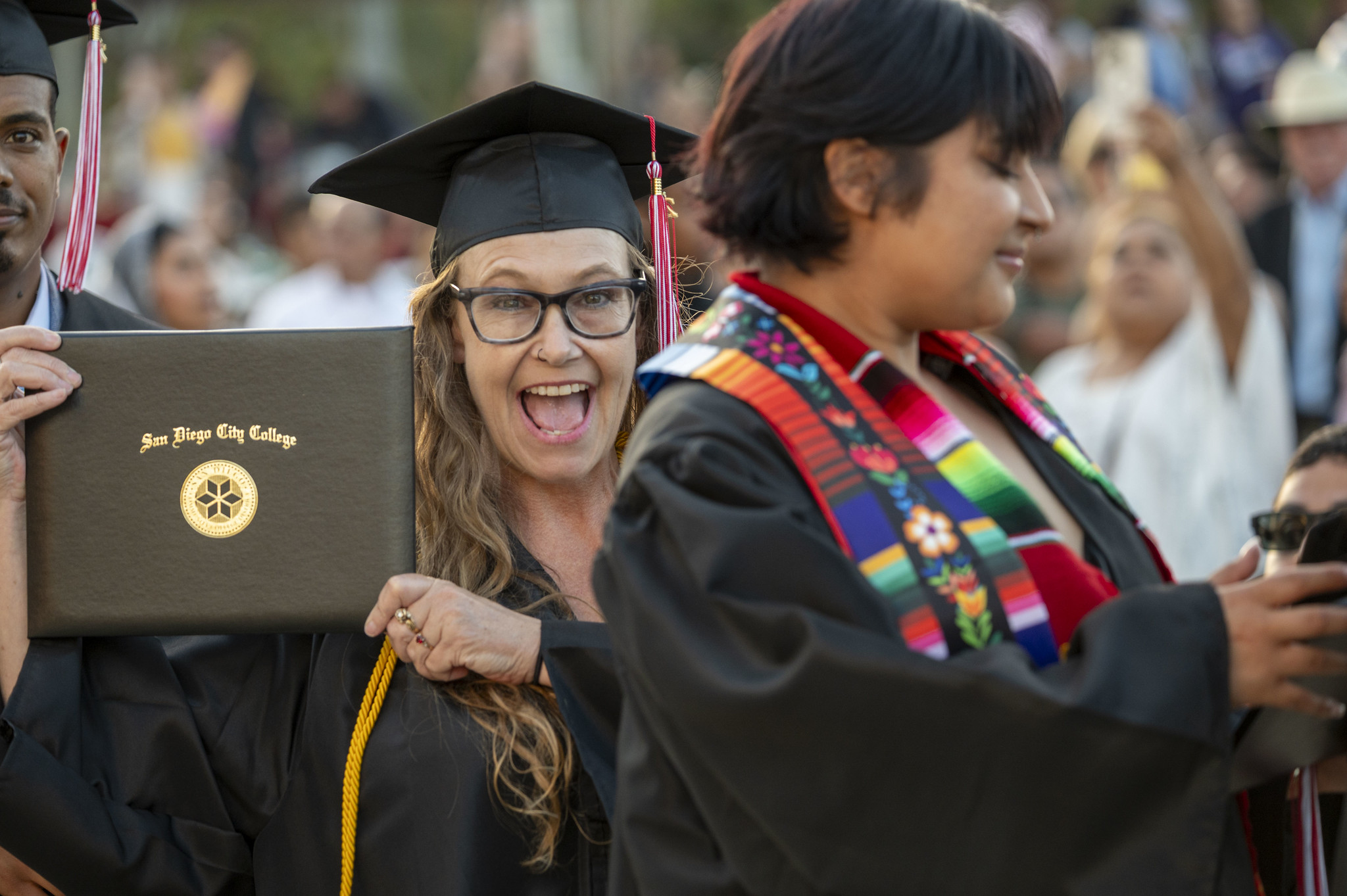 
A graduate is in the audience smiling and holding up her degree.
