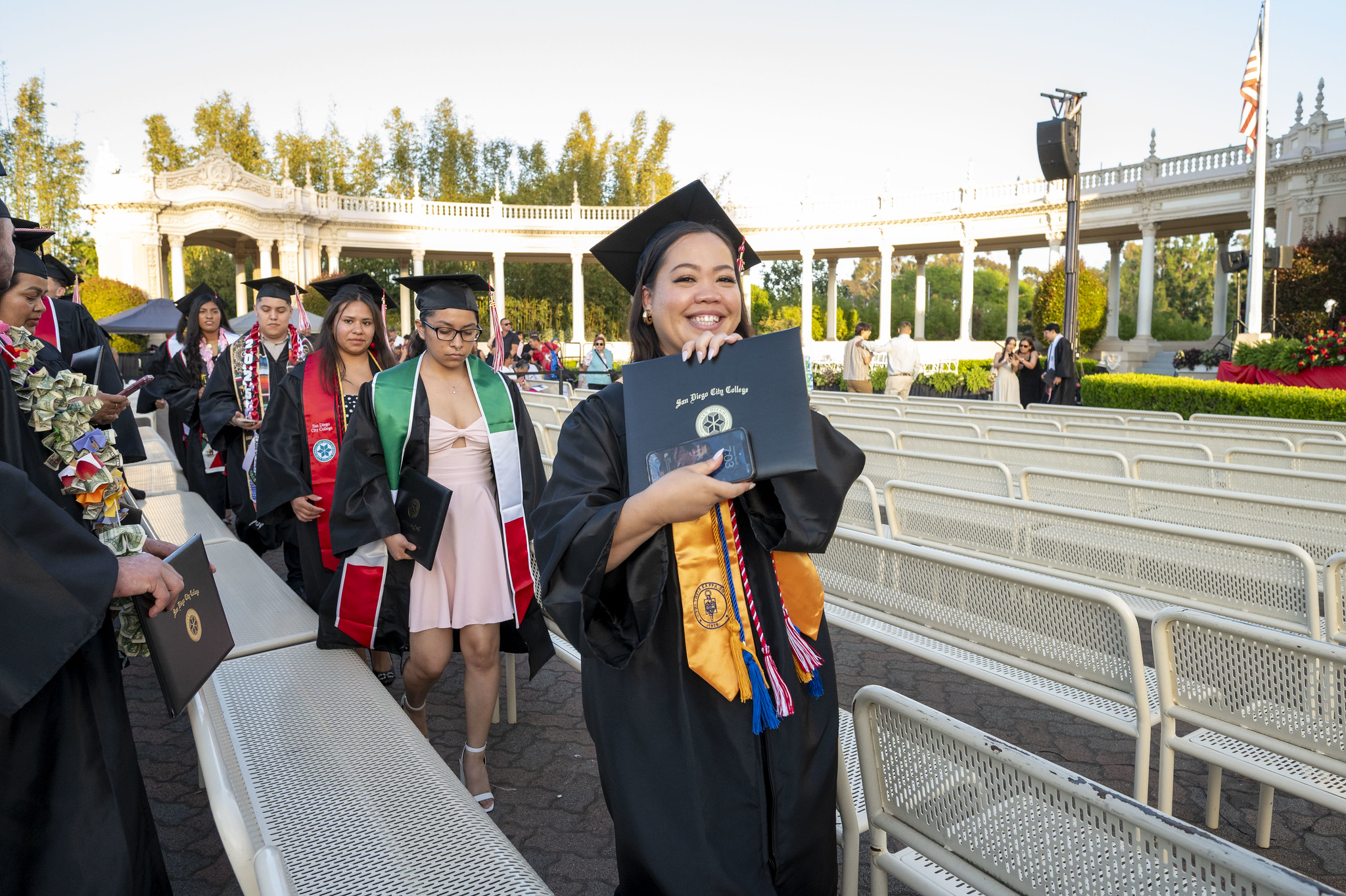 
A graduate is in the audience smiling and holding up her degree.
