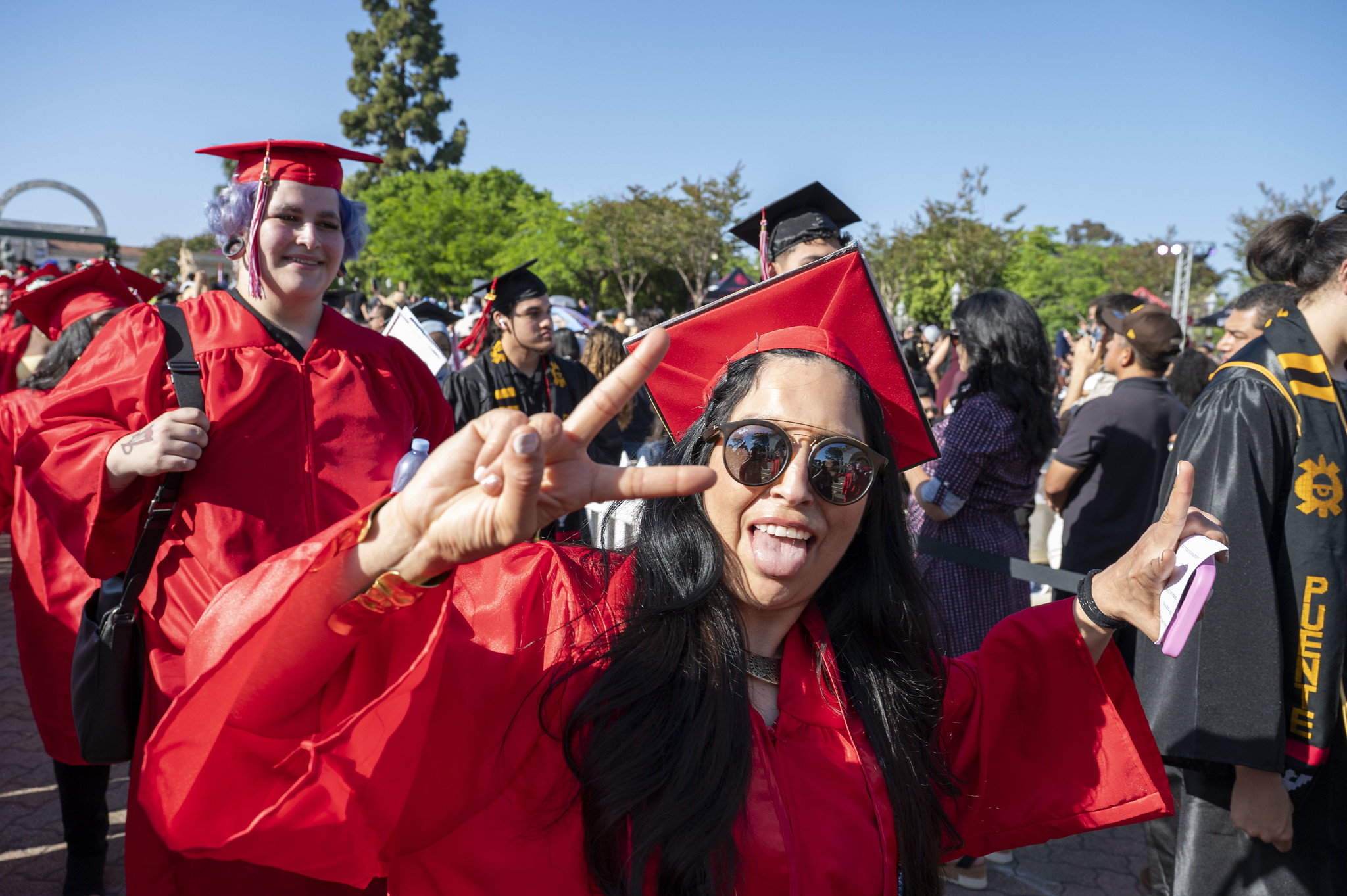 
A graduate in a red cap and gown giving a peace sign.
