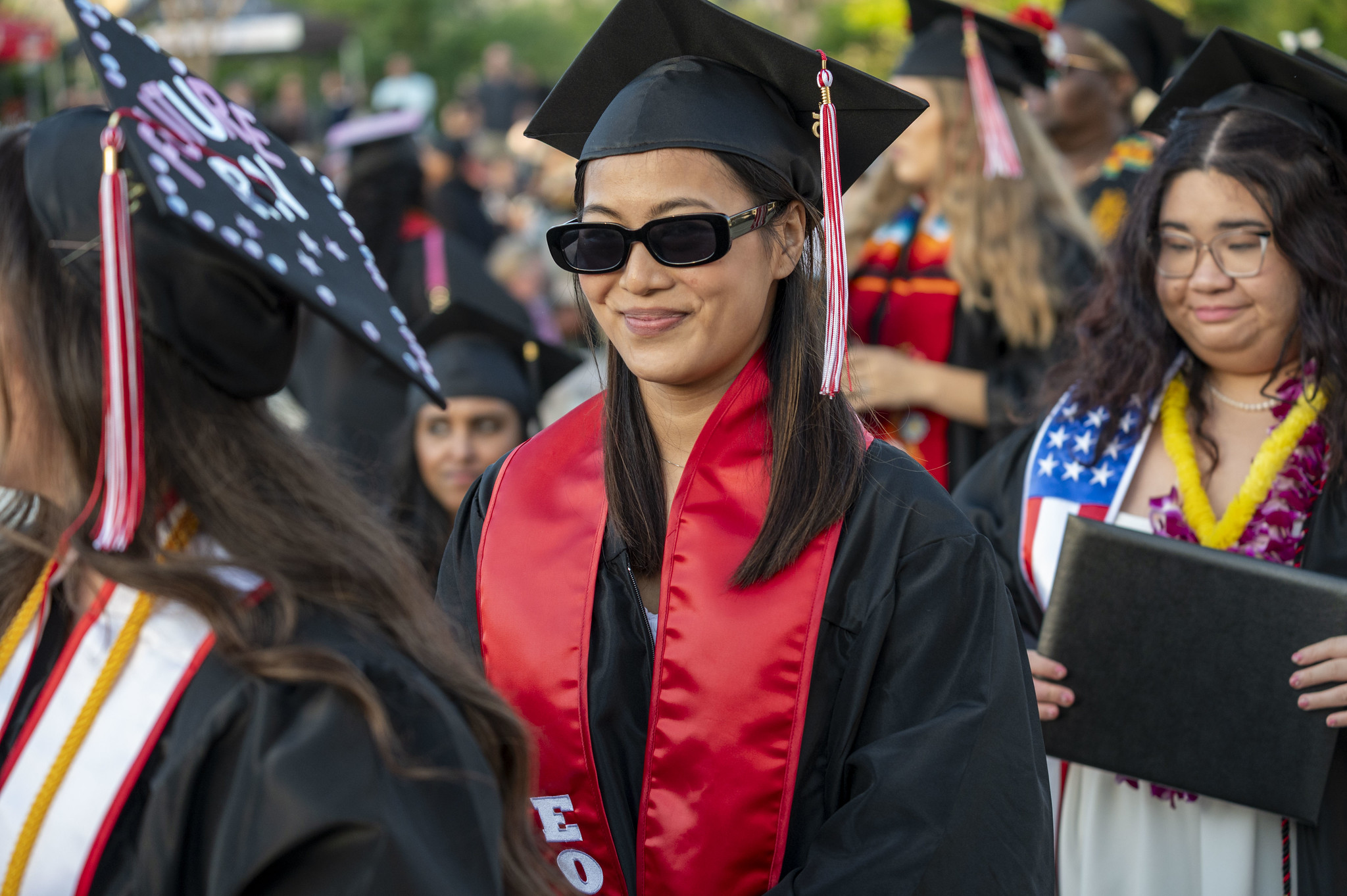 
A graduate in a black cap and gown with a red sash.
