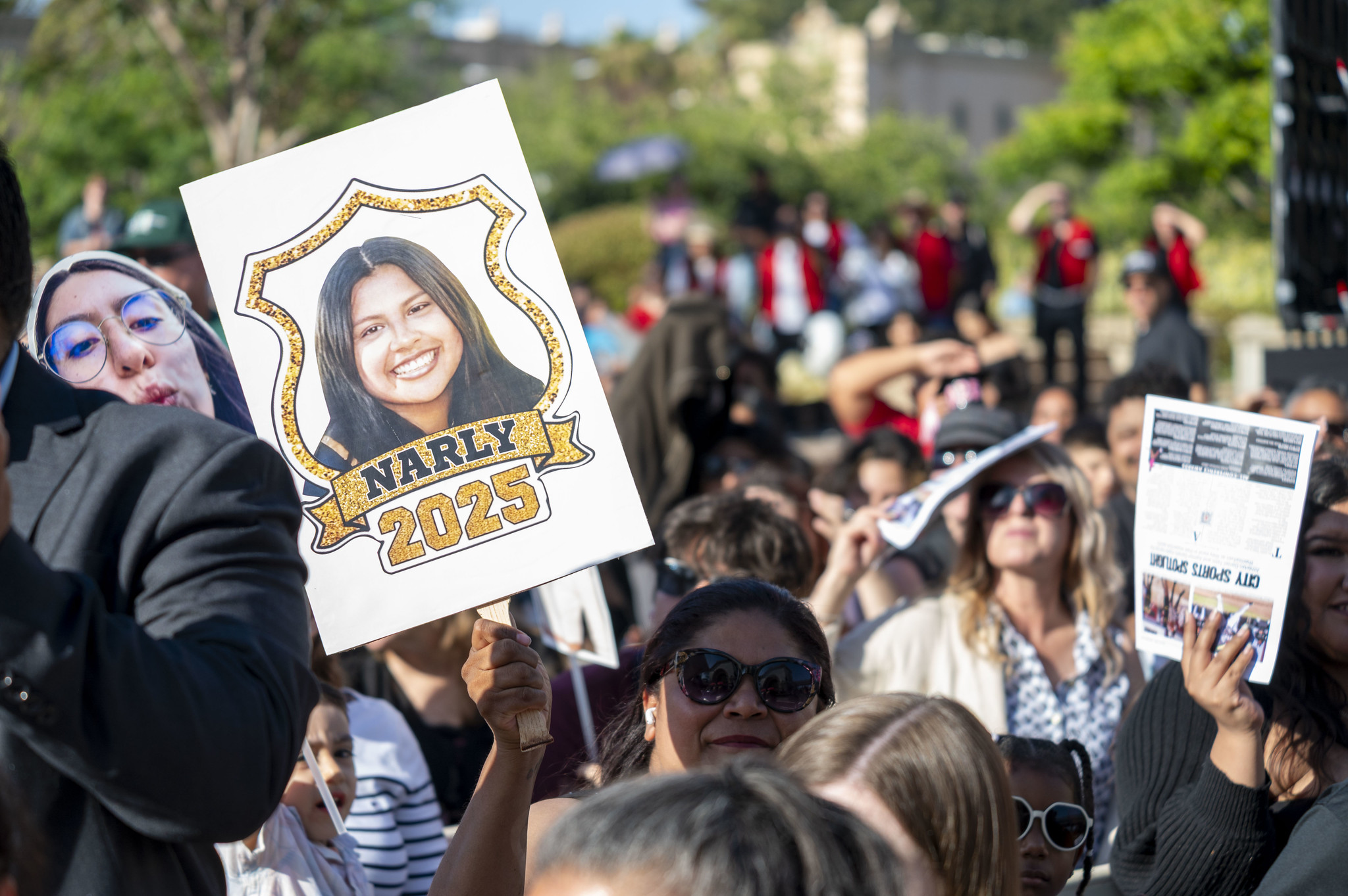 
A proud family member holds up a sign with a graduate's picture on it.
