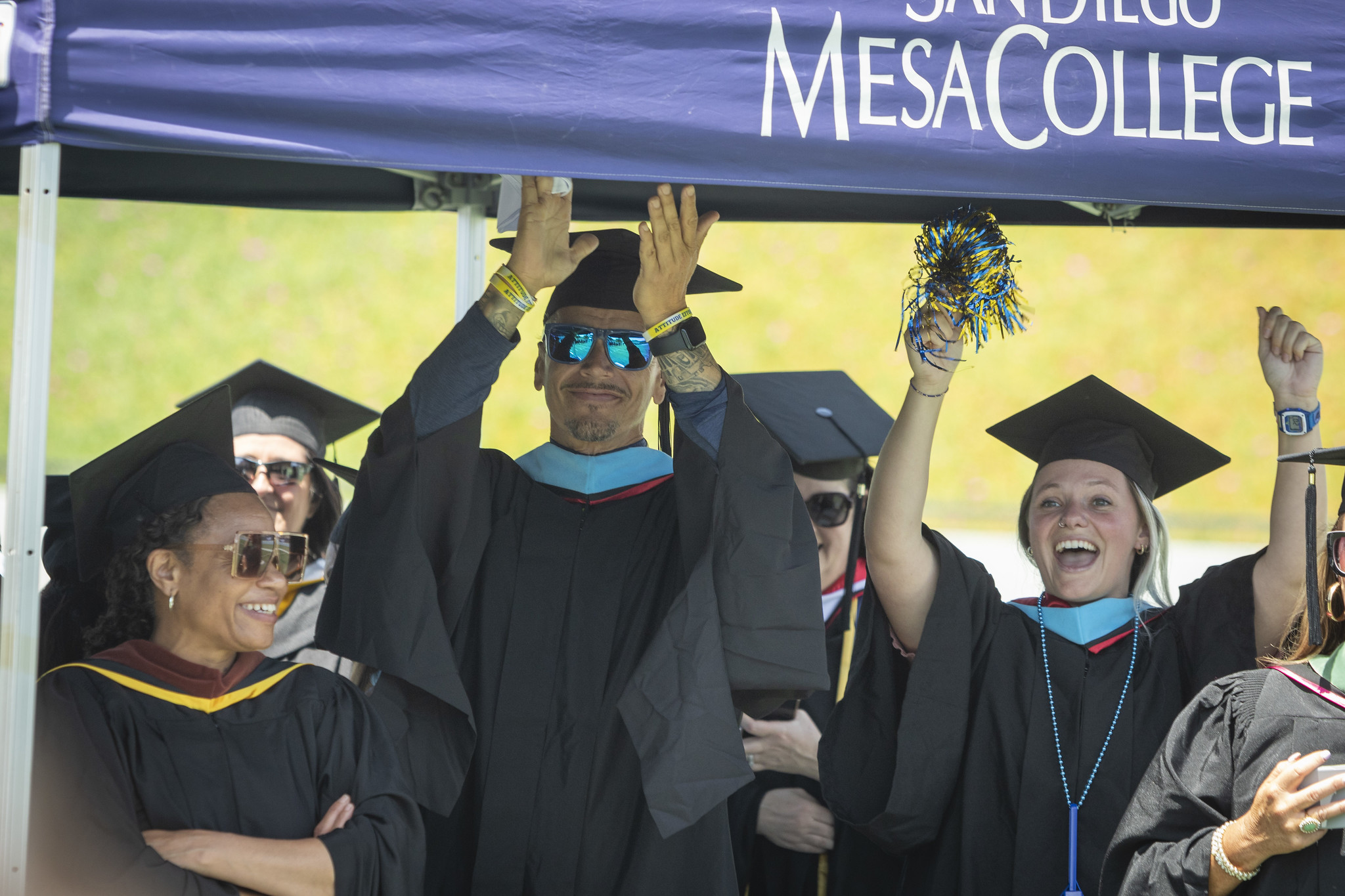 
Faculty in black graduation caps and robes cheer on the graduates.
