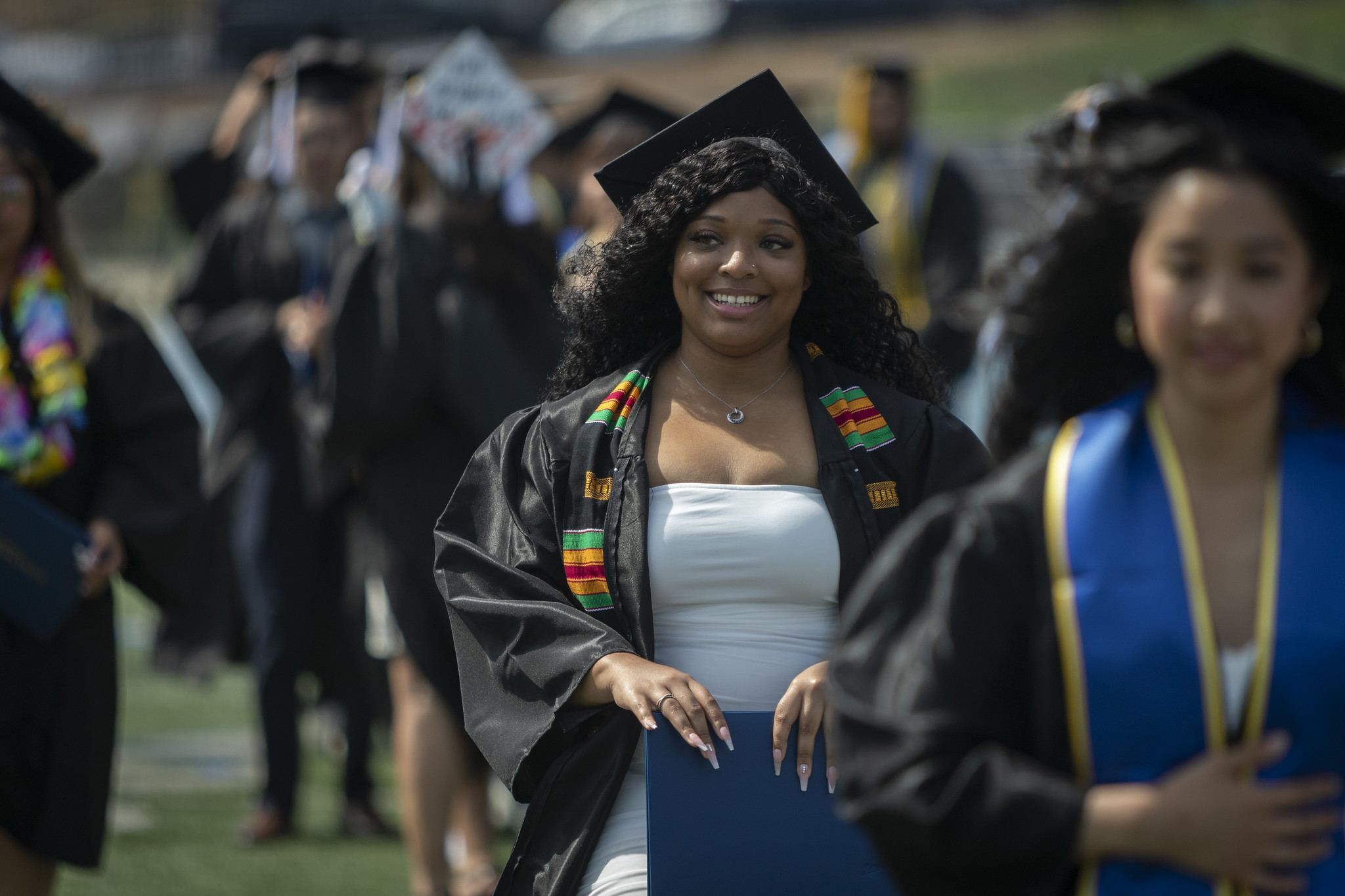 
A graduate smiling in the crowd, holding her degree.
