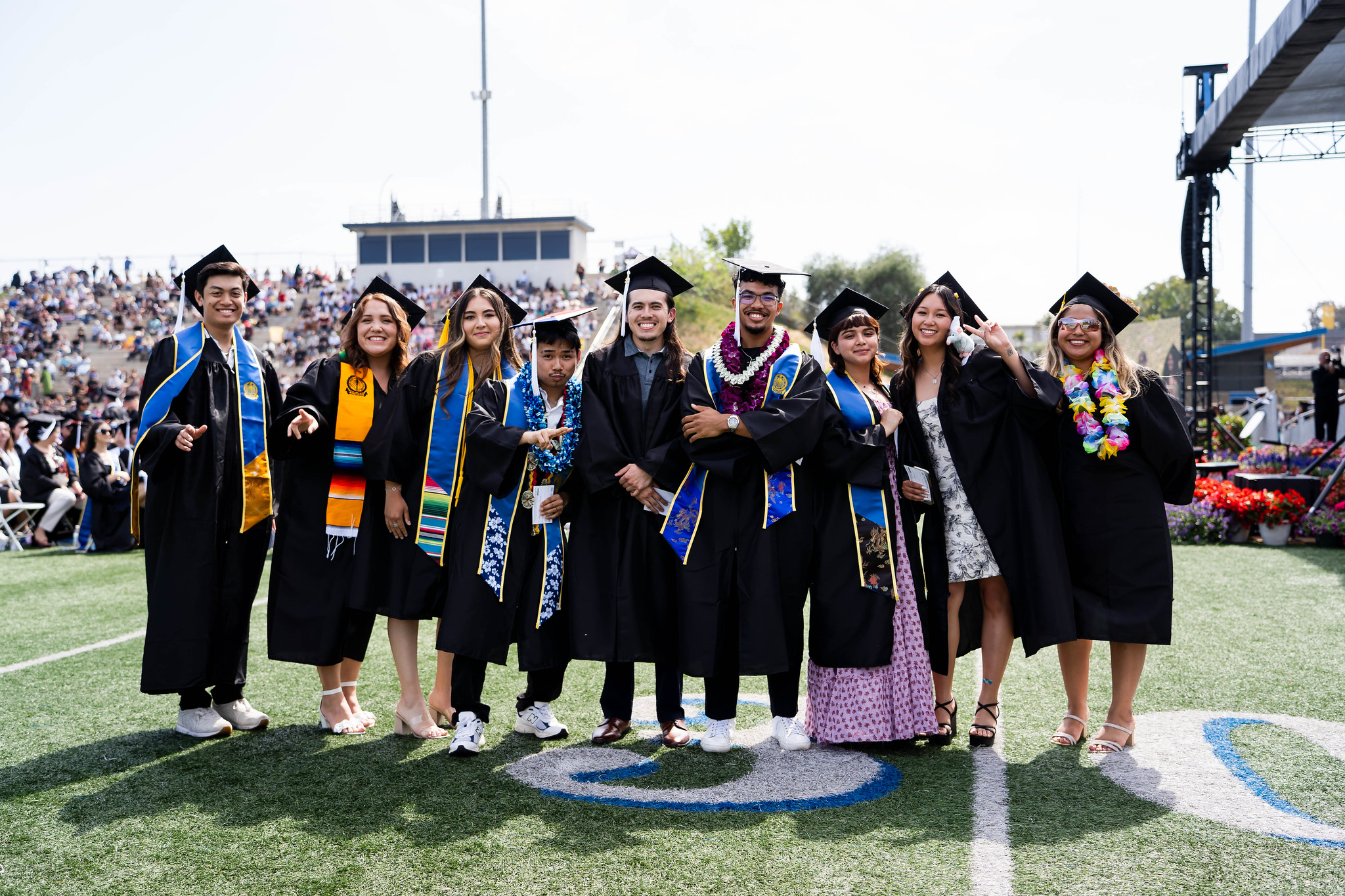 
Nine graduates line up for a group photo on the field at commencement.
