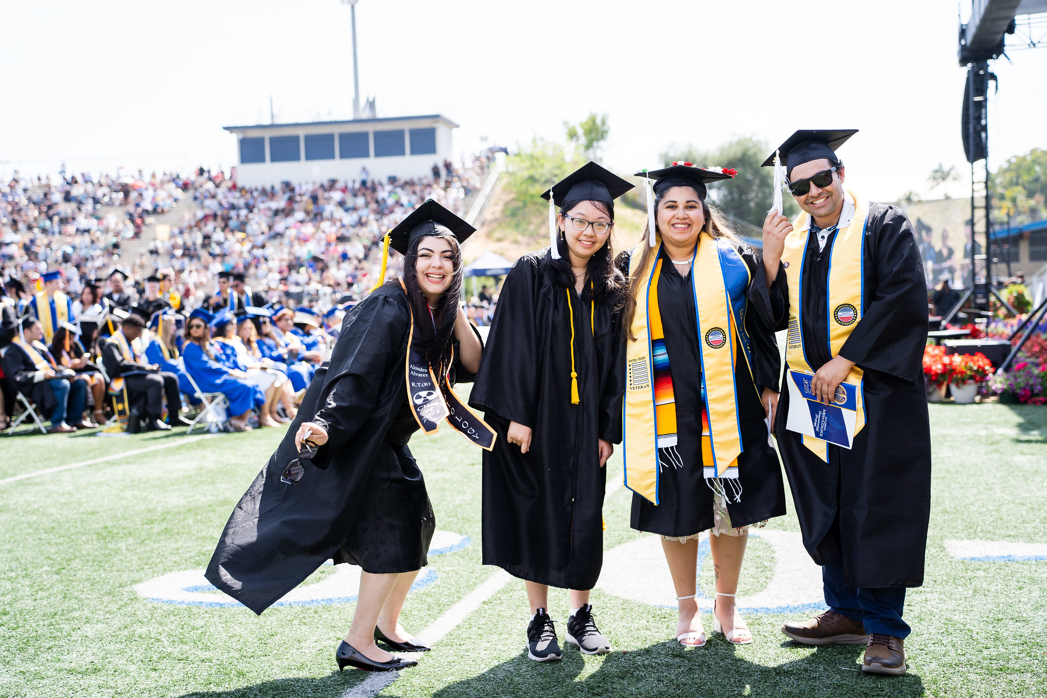 
Four graduates line up for a group photo on the field at commencement.
