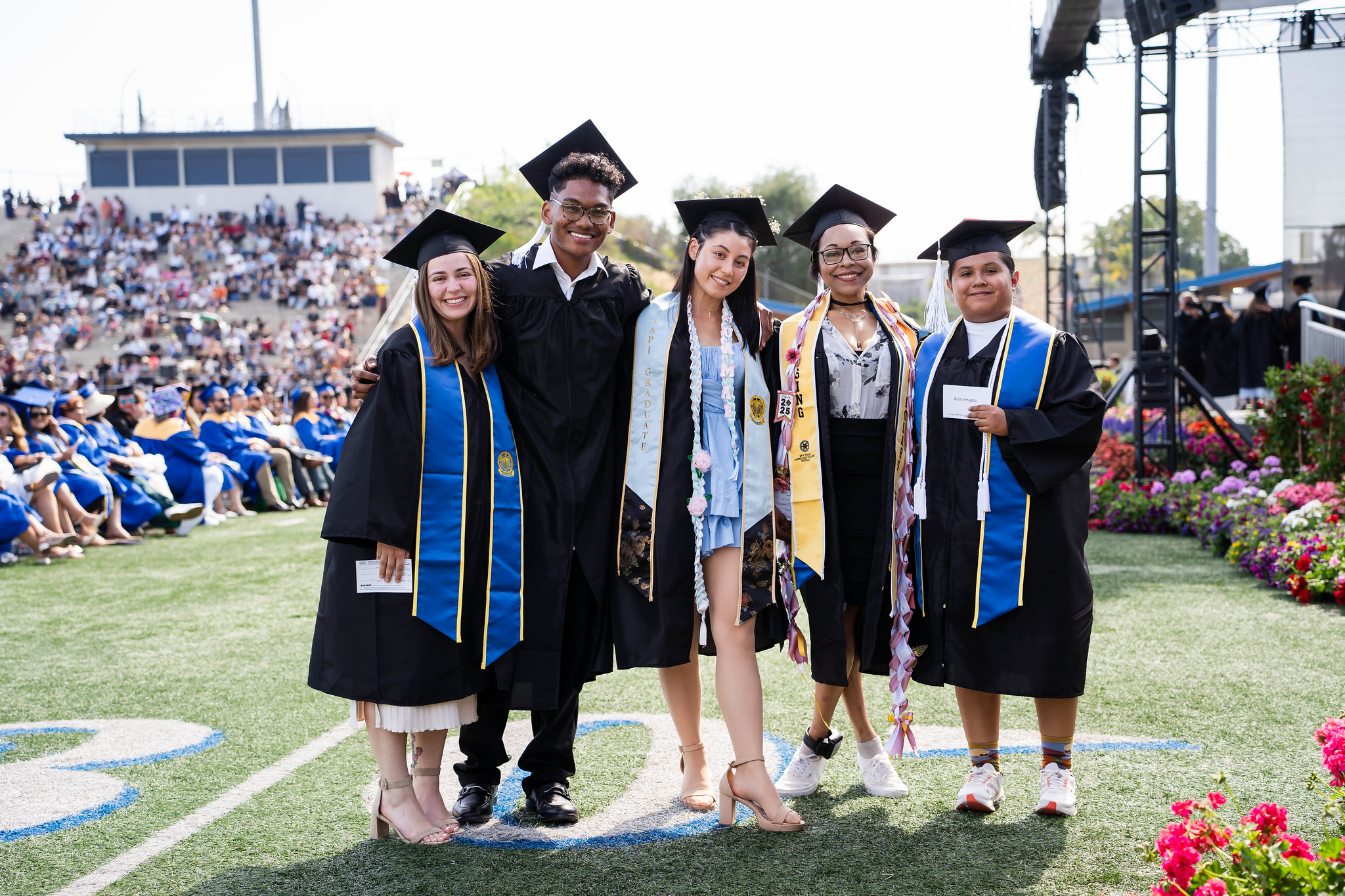 
Five graduates line up for a group photo on the field at commencement.
