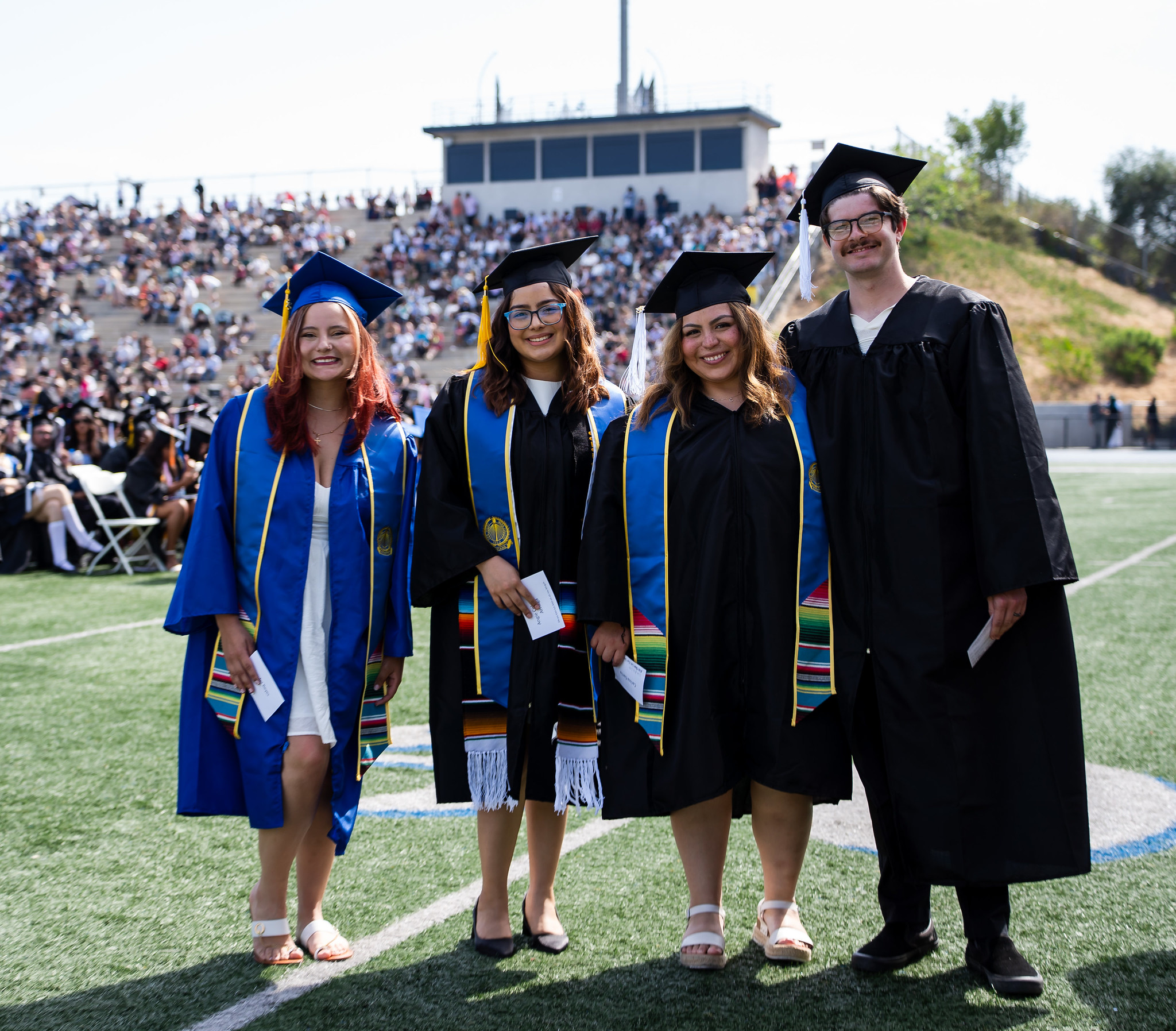 
Four graduates line up for a group photo on the field at commencement.
