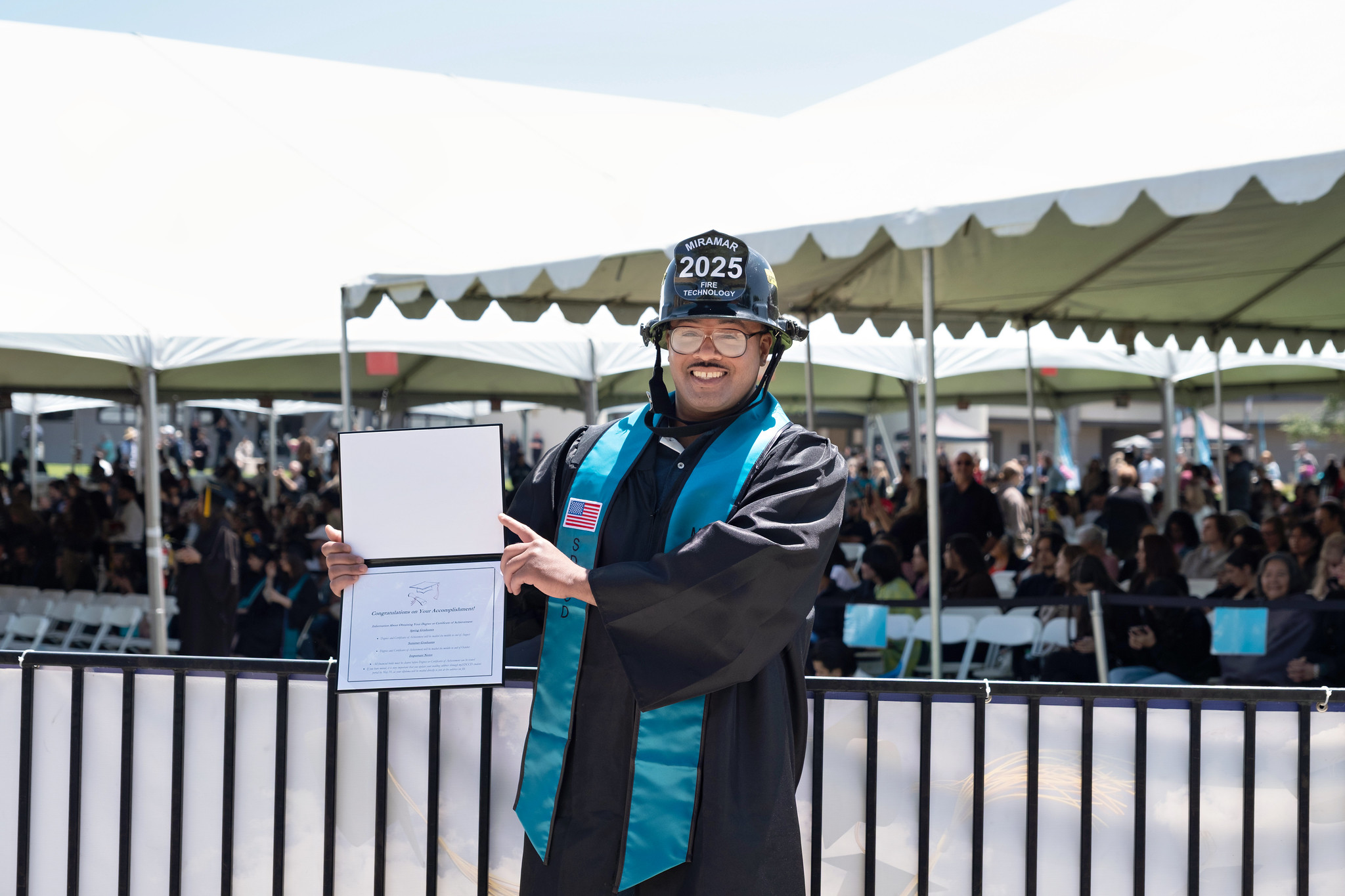 
A fire academy student in a black fire helmet holds up his degree.
