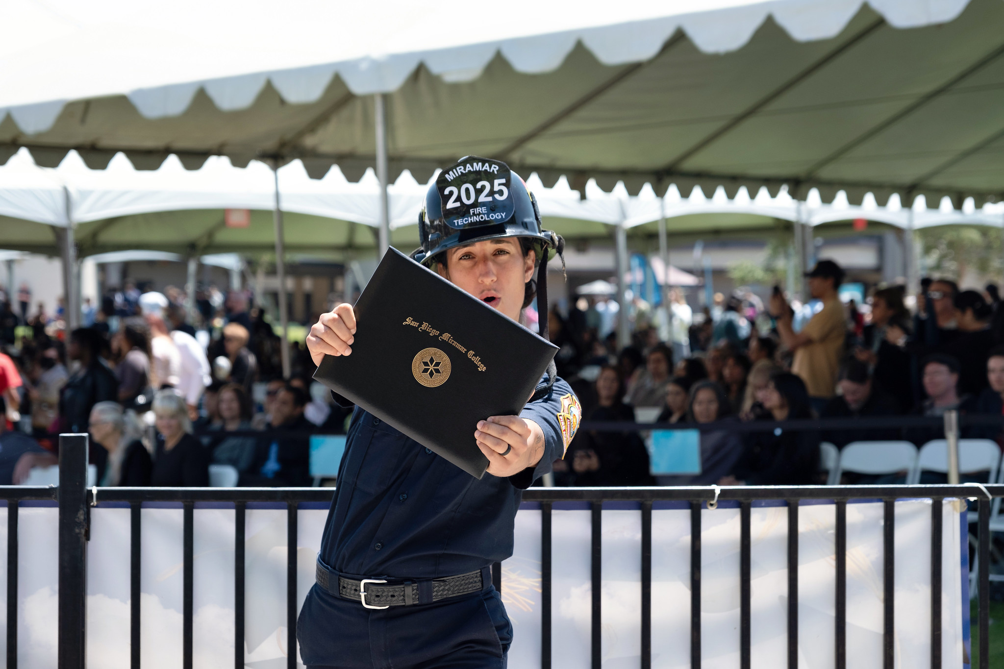
A fire academy student in a black fire helmet holds up his degree.
