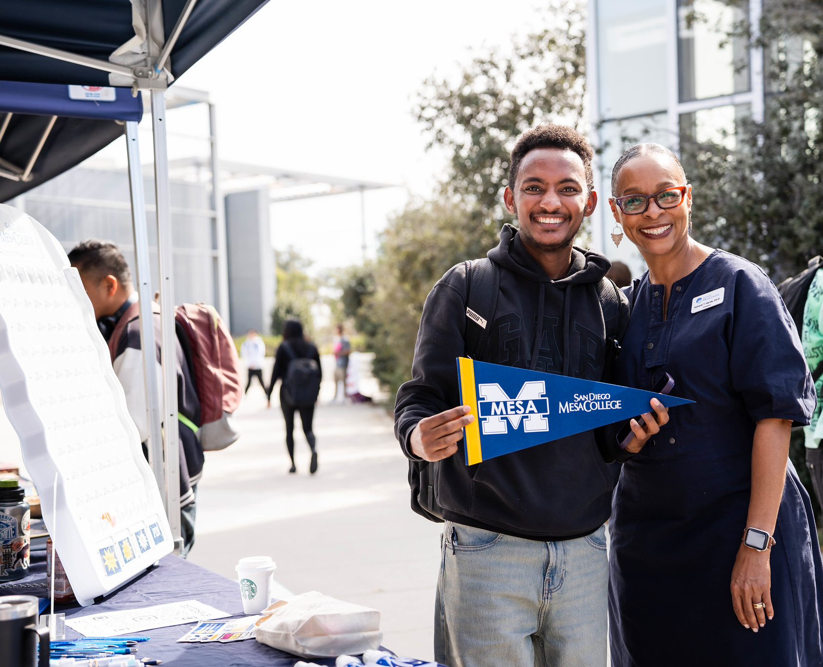 
President Ashanti Hands with a student holding a Mesa College pennant.
