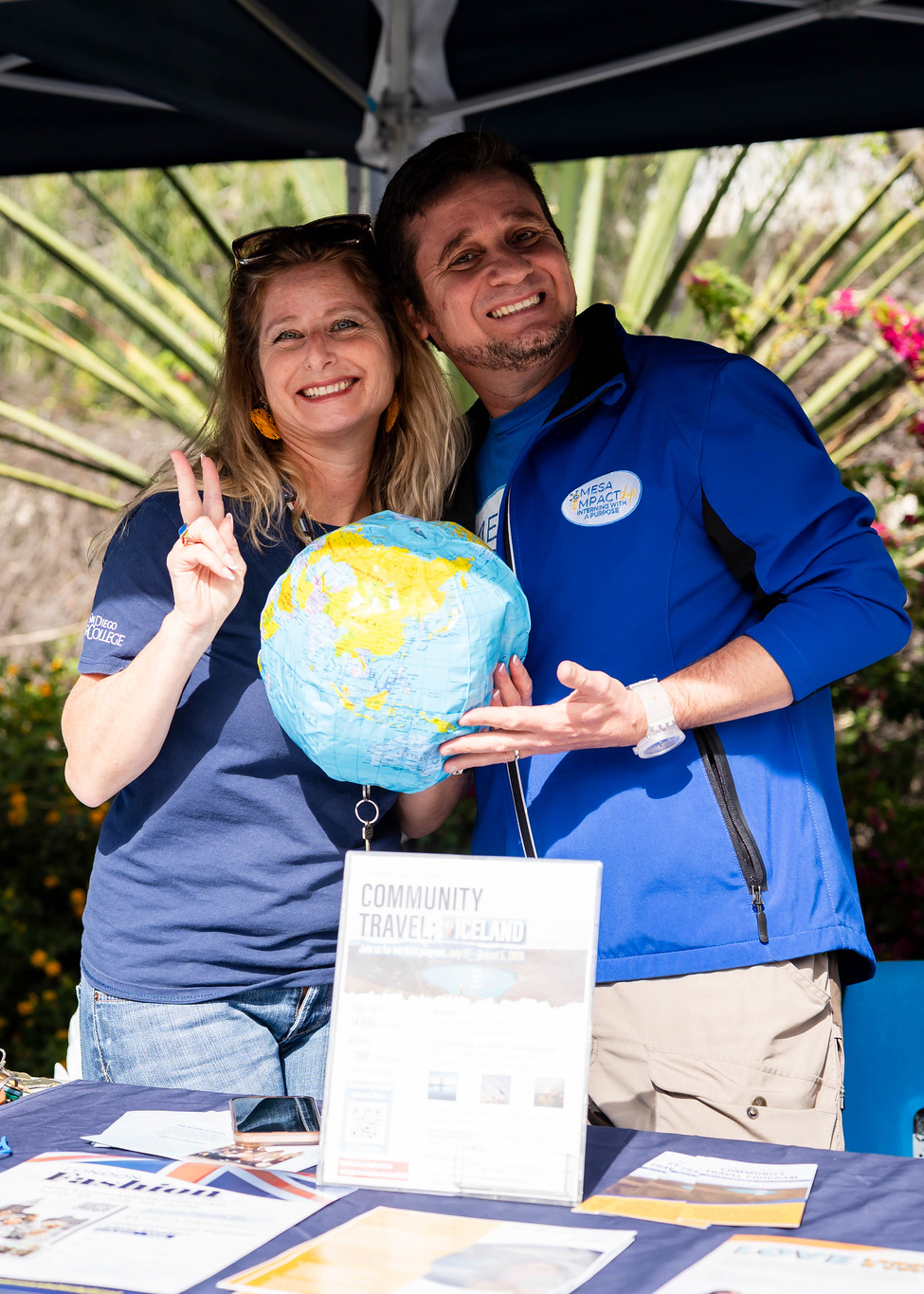 
Two people at the travel welcome booth hold up a blow up globe.
